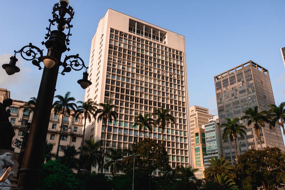 Câmara Municipal SP. — Explore the contemporary architecture of a bustling city with tall skyscrapers and palm trees.